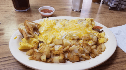 A plate of cheesy omelette with toast and seasoned potato cubes, accompanied by a small cup of salsa.